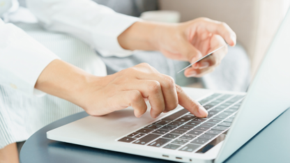 Primo piano di mani, una digita sulla tastiera di un computer portatile mentre l'altra stringe una carta di credito